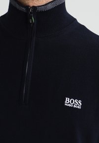 Marinblå kvartdragare i ribbat material, med en texturerad krage, en liten vit broderad "BOSS"-logotyp och svart dragkedja.