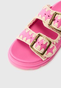 Rosa sandal laget av gummi med flettede beige detaljer og to gullspenner. Har en teksturert såle og utskjæringer på stroppene.