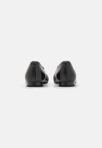 Scarpe in pelle nera con una finitura liscia, tacco basso e punta rotonda. Presentano dettagli di cucitura discreti e una silhouette elegante.