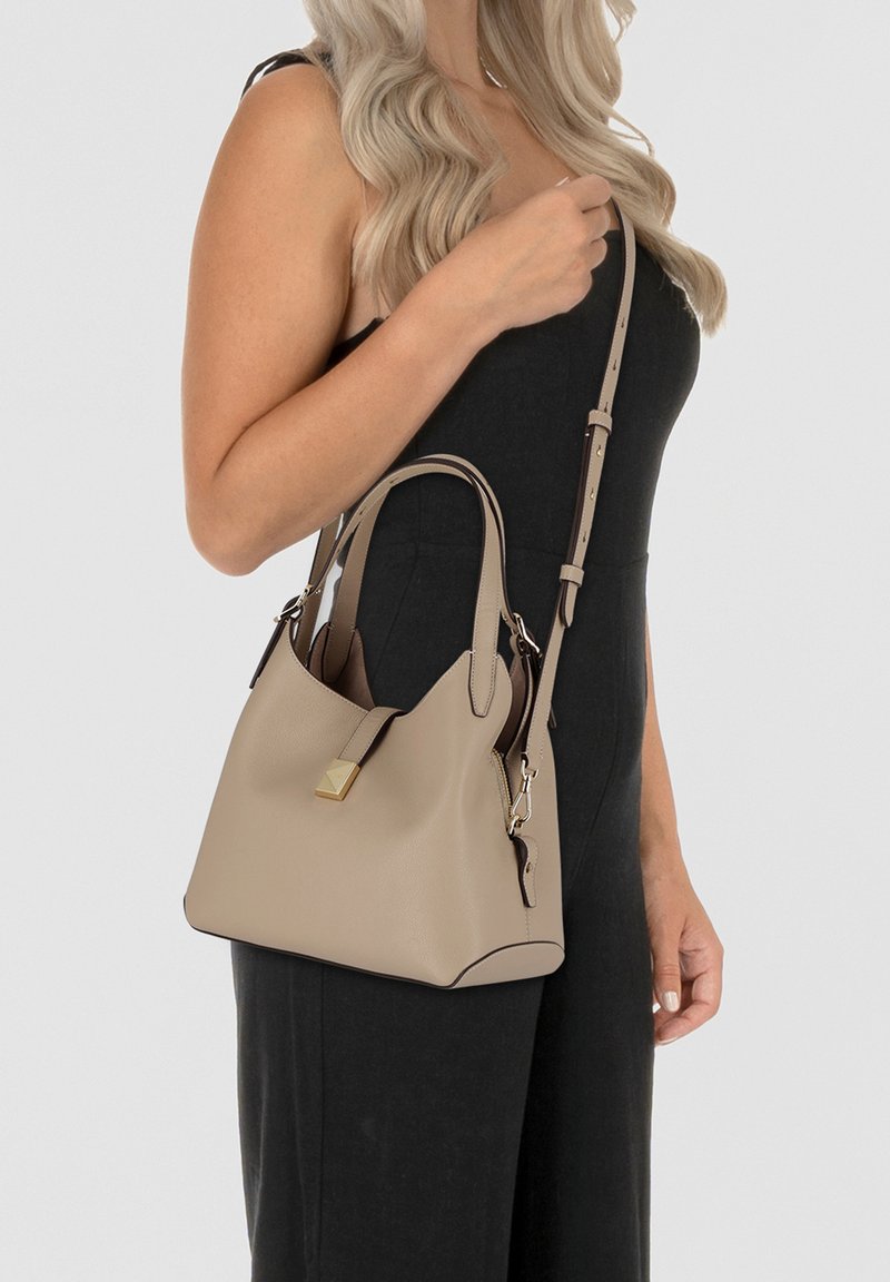 Beige leather handbag with short handles and an adjustable crossbody strap. Features gold hardware and a zippered compartment.