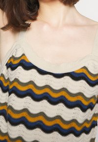 Pletené tílko s vroubkovaným výstřihem zdobeným vlnitými pruhy v béžové, černé, modré, zelené a žluté barvě. Texturovaná, lehká látka.