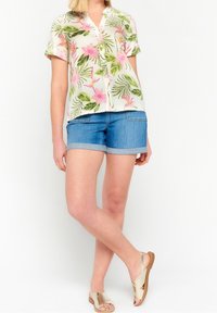 Floral short-sleeve button-up shirt with pink and green patterns, paired with rolled denim shorts and beige flat sandals.