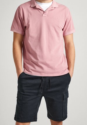 Hellrosa Baumwoll-Poloshirt mit Kragen und einem Knopf, kombiniert mit dunkelblauen Cargo-Shorts mit Seitentaschen und Kordelzug in der Taille.