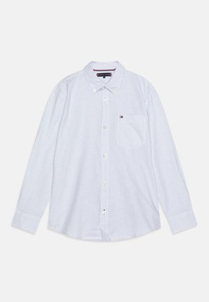 Chemise blanche à manches longues avec rayures verticales bleu clair, col boutonné, poche poitrine et petit logo Tommy Hilfiger sur la poche.