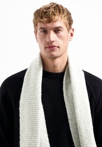 Hellgrau gestreifter Schal aus weichem Material, locker um den Hals drapiert, kombiniert mit einem schwarzen strukturierten Pullover.