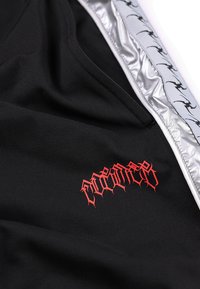 Μαύρο ύφασμα με κόκκινο λογότυπο σε γοτθικό στιλ και ασημένια λωρίδα με επαναλαμβανόμενο μοτίβο μαύρου δράκου κατά μήκος της άκρης.