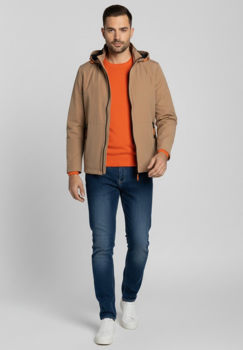 Chaqueta con capucha color beige con detalles en naranja sobre un suéter naranja, combinada con vaqueros azules y zapatillas blancas. Material liso y ligero.