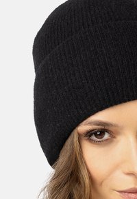 Gorro negro de punto hecho de lana suave, con una textura acanalada y un diseño ajustado. El sombrero es simple y sin costuras, sin logotipos visibles.