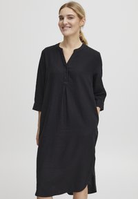 Robe en lin noir avec un décolleté en V, patte de boutonnage, manches trois-quarts, poches latérales et un ourlet légèrement arrondi. Texture lisse.
