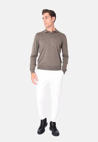 Polo shirt lungo a maniche con colletto di colore verde oliva, con tre bottoni, abbinato a pantaloni bianchi e sneakers nere alte.