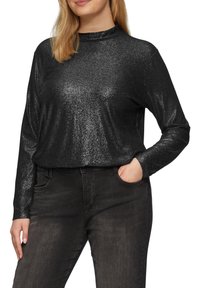 Zwarte lange mouwen top met een hoge nek, gemaakt van glinsterend materiaal, heeft een ontspannen pasvorm en een gladde textuur, gecombineerd met donkere jeans.