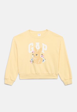 Sweat-shirt jaune à manches longues avec le texte blanc "GAP", une illustration détaillée d'un lapin, et de petites fleurs roses et bleues sur le devant.