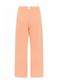 Pantalones anchos de melocotón claro con un tejido texturizado, cintura elástica y una pequeña etiqueta en la parte trasera. Diseño limpio y minimalista.
