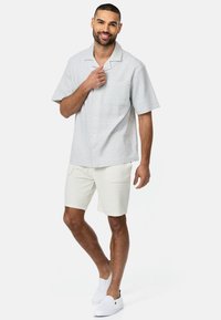 Lyhythihainen, vaaleanharmaa napp shirt, jossa on hienovarainen kuvio ja rintatasku, yhdistettynä valkoisiin teksturoituihin shortsit ja liukuvaat. 