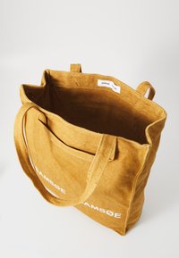 Sennepsgul lerret tote bag med robuste håndtak, innvendig merkelapp og trykt logo på forsiden. Åpen toppdesign for enkel tilgang.