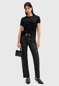 Top corto nero a maniche corte con finitura testurizzata, abbinato a pantaloni in pelle nera aderenti. Gli accessori includono una piccola borsa nera e sandali con cinturini.