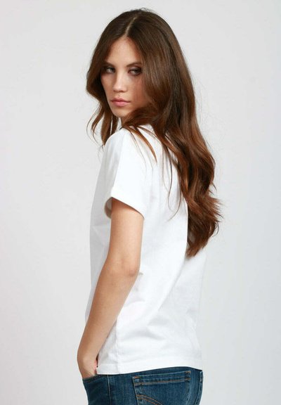 T-shirt bianca in cotone con maniche corte arrotolate, colletto rotondo e vestibilità comoda, abbinata a jeans blu scuro. Sfondo neutro.