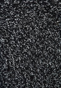 Tissu tricoté noir et blanc avec un motif texturé, présentant de petites fibres entrelacées créant un effet moucheté.