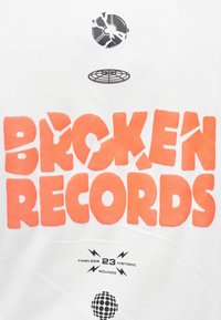 Λευκό ύφασμα με έντονα, ακανόνιστα πορτοκαλί γράμματα «BROKEN RECORDS» και μαύρα γραφικά ενός ραγισμένου βινυλίου και λογότυπου σε κυκλικό σχήμα από κάτω.