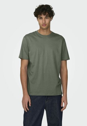 Camiseta verde oliva de manga corta hecha de algodón, con cuello redondo y corte relajado. Jeans con acabado de mezclilla oscura visibles por debajo.