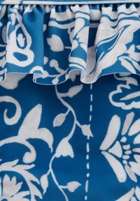 Zila auduma ar baltu ziedu rakstu, kam ir viļņota mala. Tekstūra ir gluda, ar smalkiem ziedu dizaina elementiem.