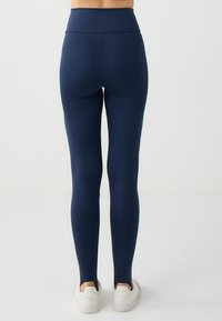Leggings blu navy con vita alta, texture liscia e forma aderente, abbinate a sneakers bianchi. Nessun motivo o accentuazione visibile.