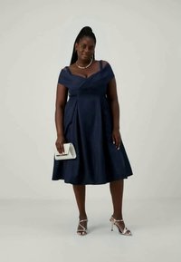 Μπλε φόρεμα με off-shoulder σχέδιο, με εφαρμοστό κορσάζ και φουσκωτό φούστα, συμπληρωμένο με ασημένιες αγκράφες και λευκή τσάντα.