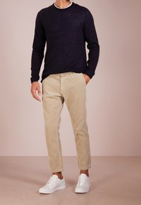 Granatowy sweter dzianinowy, beżowe spodnie sztruksowe, białe sneakersy. Sweter ma prążkowane mankiety; spodnie mają pionowe paski. Casualowy zestaw.
