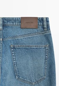 Blå denimjeans baglomme med synlige syninger og en brun lædermærkat med teksten "Massimo Dutti" over linningen.