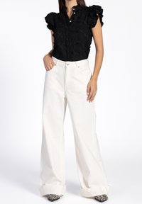 Blouse noire brodée avec manches courtes à volants, associée à un jean blanc taille haute à jambes larges, avec une coupe décontractée et des poignets retroussés.