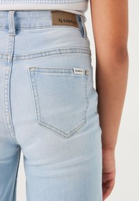 Hellblaue Denim-Jeans mit einer Gesäßtasche, die ein gewebtes Etikett trägt. Das Design umfasst Standardnähte und einen geraden Schnitt.