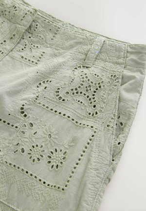 Jasnozielony materiał z detalicznymi haftami, prezentującymi kwiatowe wzory, wycięcia i teksturowane akcenty. Wzór zawiera szyte sekcje.