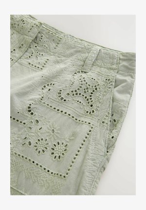 Jasnozielony materiał z detalicznymi haftami, prezentującymi kwiatowe wzory, wycięcia i teksturowane akcenty. Wzór zawiera szyte sekcje.