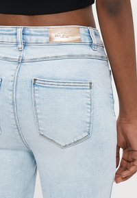 Το φως μπλε τζιν παντελόνι διαθέτει ψηλή μέση, κλασικό σχεδιασμό με πέντε τσέπες και καφέ δερμάτινη ετικέτα μάρκας στη πίσω μέση.