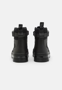 Black ankle boots with a textured finish, adjustable straps, and pull tabs at the back; rubber soles with horizontal grooves for grip.