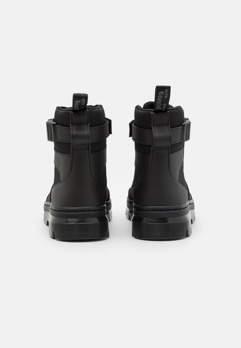 Botas negras de tobillo con un acabado texturizado, correas ajustables y tiradores en la parte posterior; suelas de goma con ranuras horizontales para mayor agarre.