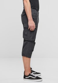 Harmaat, monitaskuiset polvipituiset cargoshortsit säädettävillä lahkeensuilla ja kevyestä kankaasta, yhdistettynä mustiin tennareihin, joissa valkoisia yksityiskohtia.