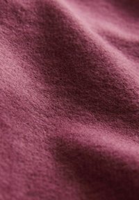 Tissu à texture douce de couleur mauve profond avec des plis visibles et une surface légèrement duveteuse, suggérant chaleur et confort.