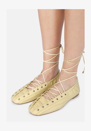 Gaišdzelteni baleta apavi ar auklu dizainu, izgatavoti no ādas, ar noapaļotu purngalu un metāla acīm auklām ap potīti.