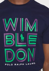 Marinblå kortärmad T-shirt med fet, flerfärgad text som stavar "WIMBLEDON" med en liten polo-spelare grafik ovanför "BLE."