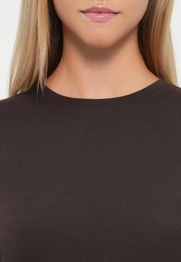 Mørkebrune, kortermede t-skjorter med rund hals. Stoffet ser glatt og tettsittende ut, uten synlige mønstre eller detaljer.