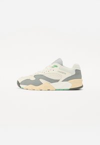 Lacoste sneakers featuring a cream upper with grey accents, mesh panels, green logo detail, and a textured beige rubber outsole.