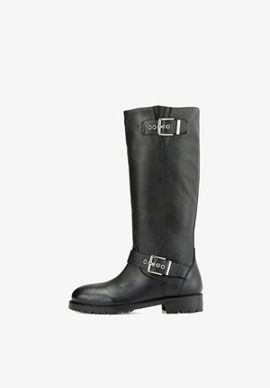 Botte noire en cuir montant jusqu'au genou avec un bout arrondi, une semelle plate en caoutchouc et deux boucles argentées décoratives sur la tige. Finition texturée.