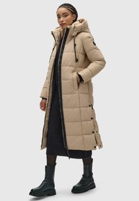 Šviesiai rudas ilgas pūkinis paltas su kvadratiniais raštais, kapisonu, priekiniais užtrauktukais ir šoninėmis kišenėmis. Dėvimas virš juodos suknelės, derinamas su juodais batais.