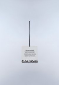 Metka odzieżowa z napisem „Special Treatment” wraz z instrukcjami pielęgnacji, zawieszona na czarnym sznurku na jednolitym jasnym tle.