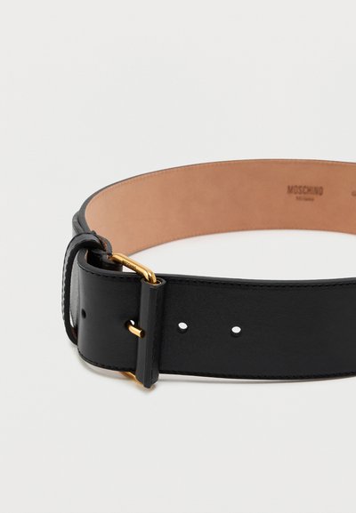 Μαύρη δερμάτινη ζώνη με λεία υφή, με χρυσή περίβλημα και πολυάριθμες τρύπες ρύθμισης. Ο εσωτερικός χώρος έχει καφέ φινίρισμα.