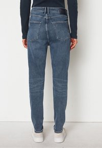 Vybledlé modré džíny s vysokým pasem a rovnými nohavicemi, pět kapes a strukturovaný pas. Zadní pohled ukazuje podrobné švy a záplatu.