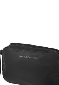 Bolsa de hombro negra de Skechers con una textura suave, cierre con cremallera y un logo destacado en un tono contrastante en la parte frontal.