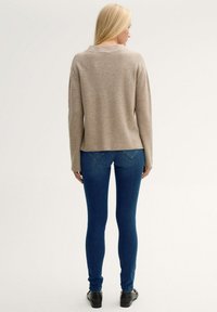 Suéter beige de corte holgado, con cuello redondo y mangas largas, combinado con jeans skinny azul oscuro y zapatos negros.