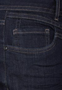 Mörka denimjeans med en slät textur, prydda med tan-färgad söm, en bakficka och en svart knapp på midjebandet.